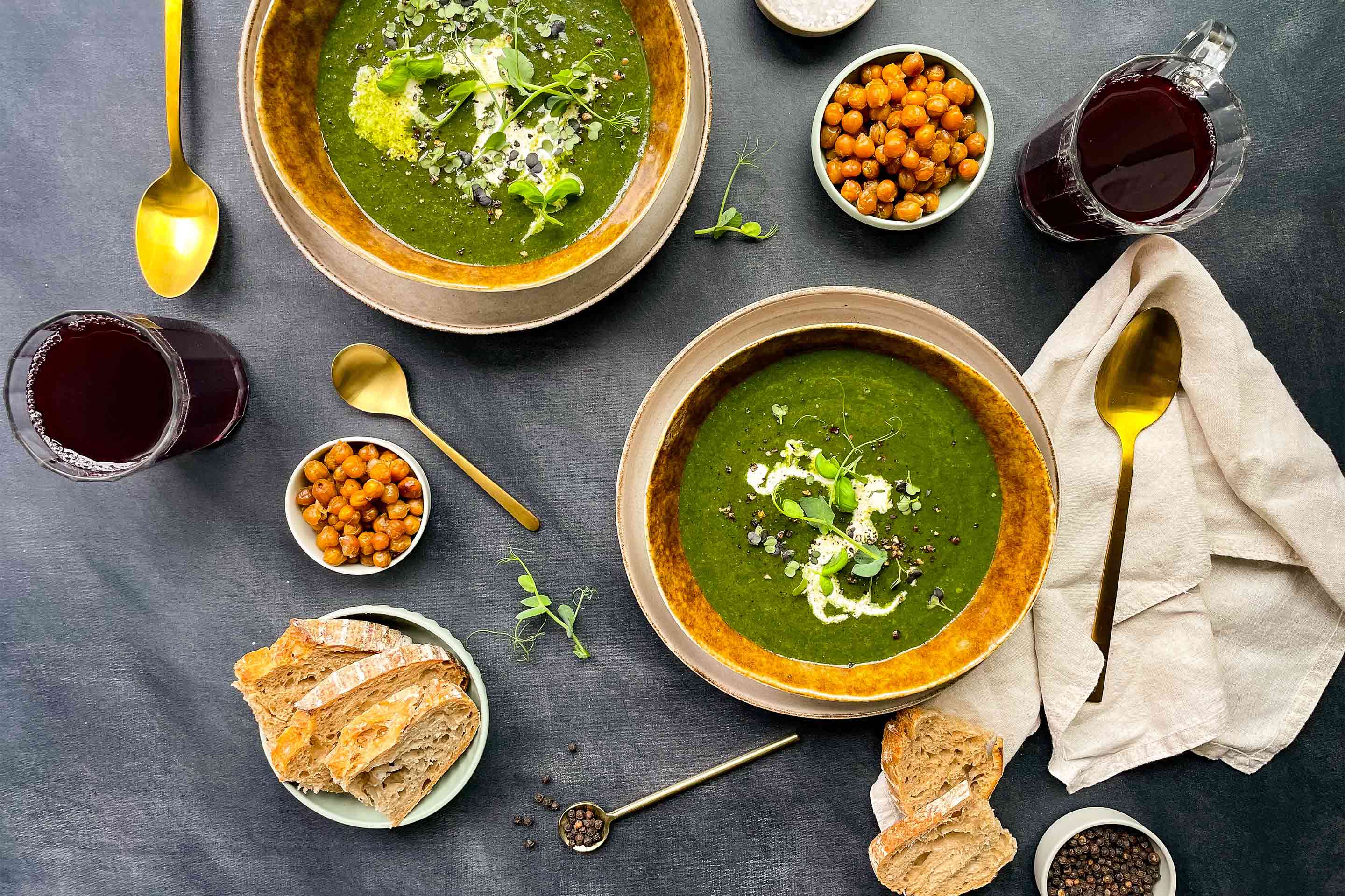 Зелена крем супа от картофи и спанак, поднесена в златисти купички, с крутони от нахут и препечени филийки хляб.