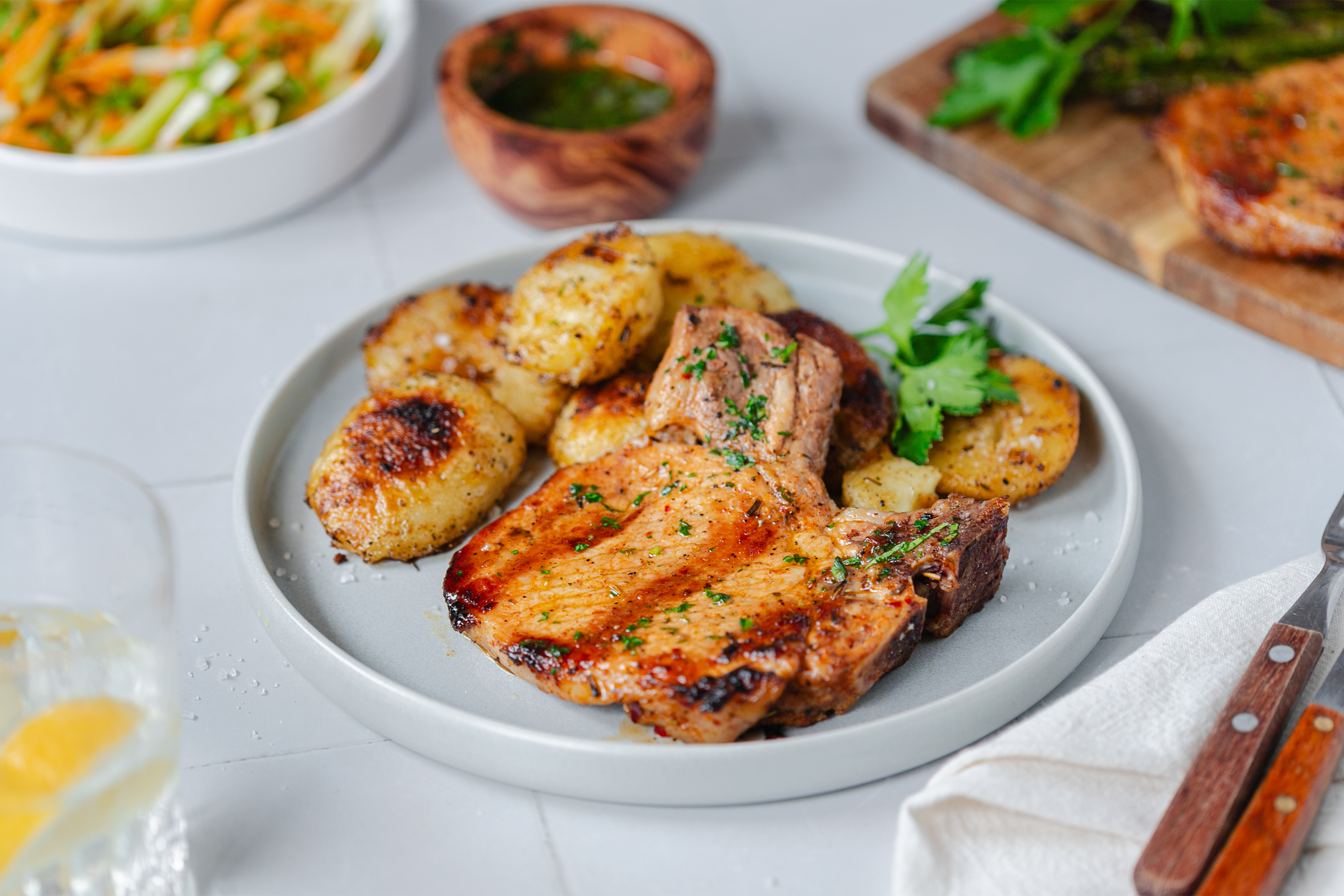 Порция пържола на скара с бейби картофи, нарязани наполовина и стръкче магданоз, поднесена в чиния с ръбче.