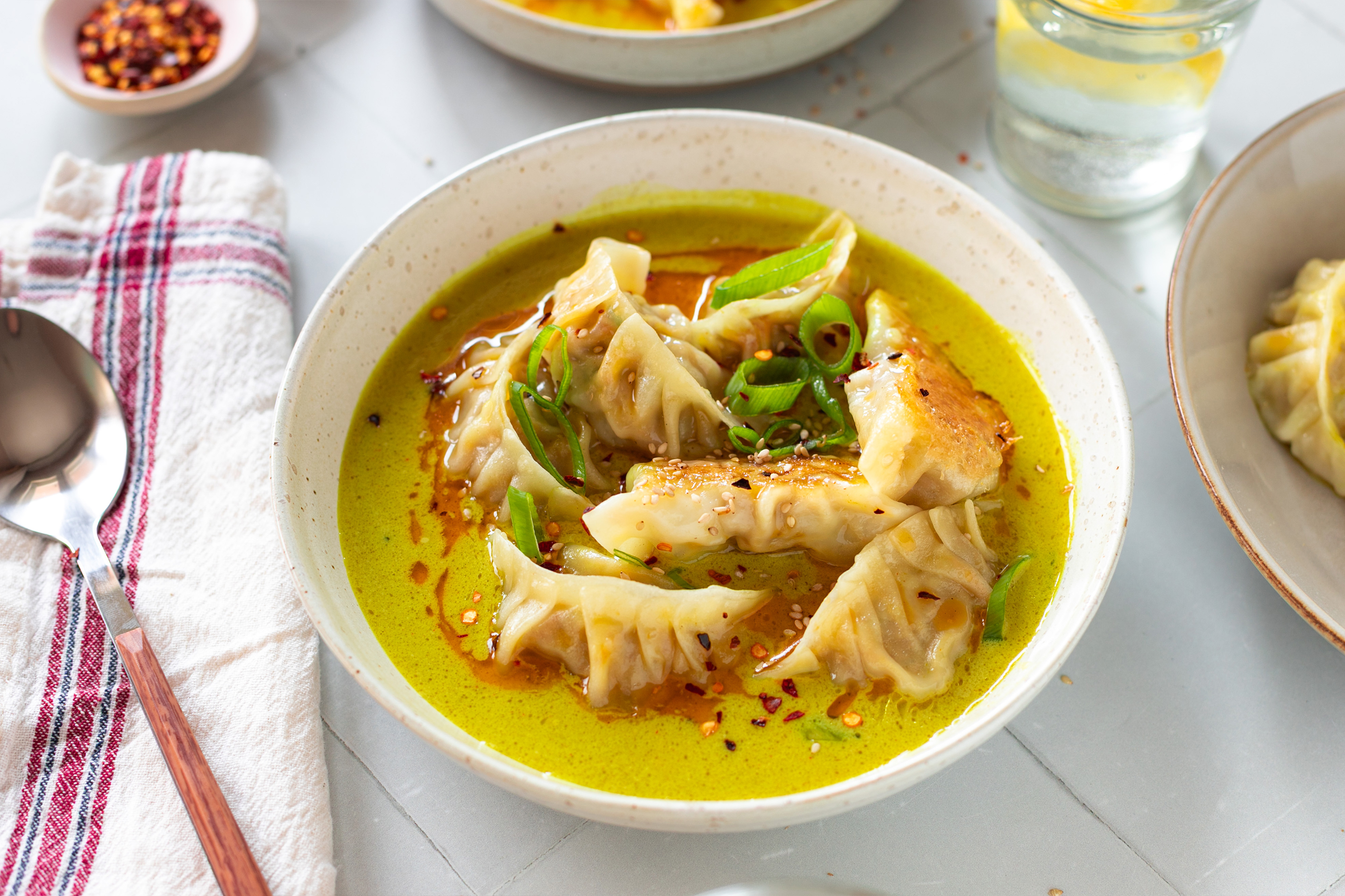 Порция японски дъмплинги гьоза в жълт къри сос, поръсена със зелен лук, сусам и чили.