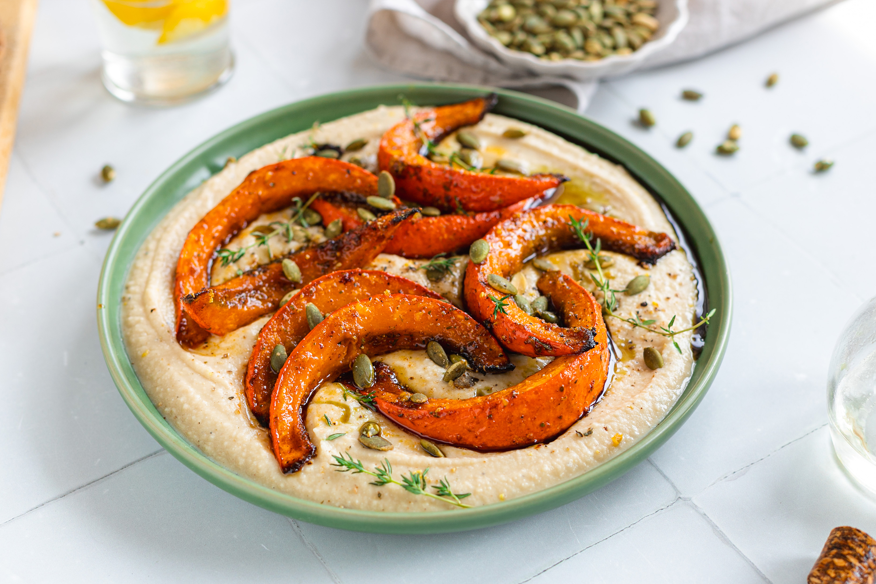 Порция хумус с резенчета печена тиква, поръсена с тиквено семе и стръкчета мащерка.