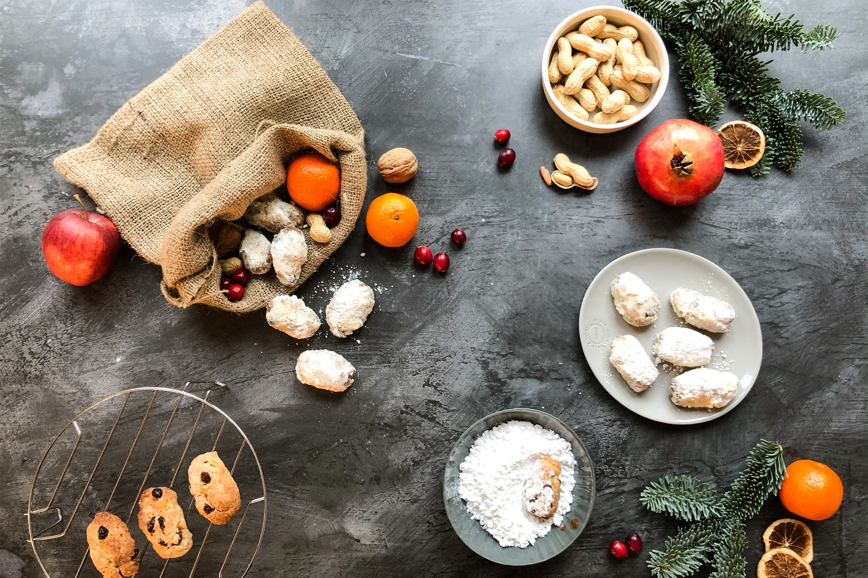 Порция дребни коледни сладкиши Щолен, аранжирана с борови клончета, портокал, нар, червени боровинки и плетено чувалче.